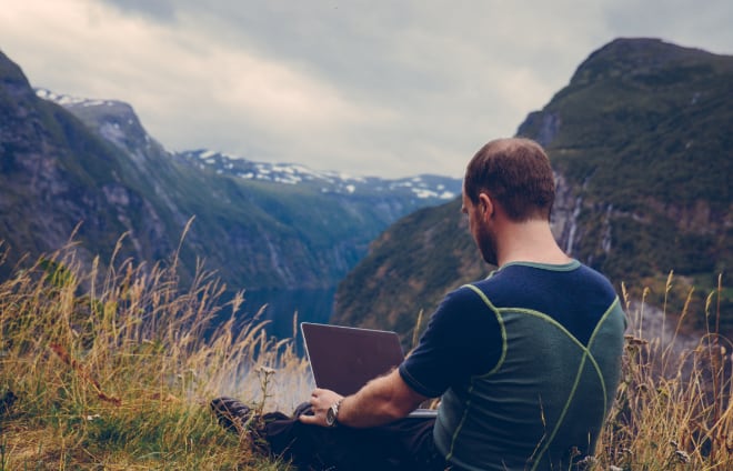 Digital nomad working on laptop on top of mountain range
