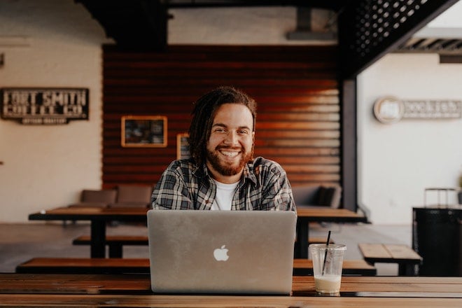 man smiling at coffee shop in front of laptop